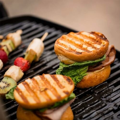 Grilled sandwiches with lettuce and fruit skewers on a grill.