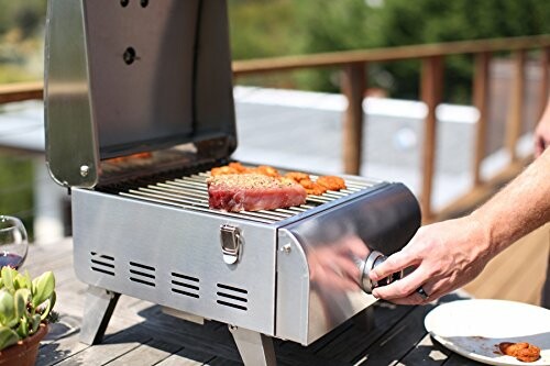 Person grilling steak and vegetables on a portable gas grill.