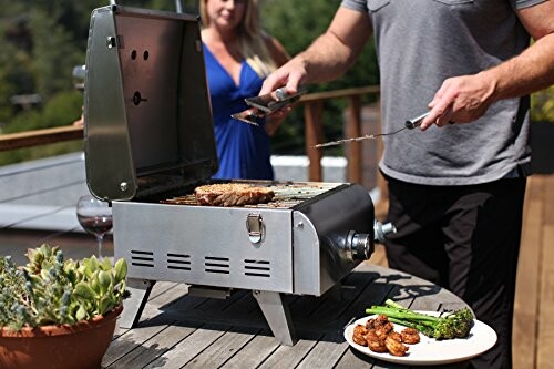 People grilling steak and vegetables on a portable grill outdoors.