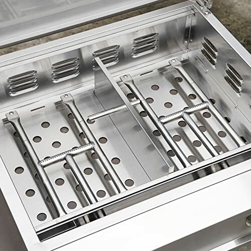 Interior view of a stainless steel grill burner with multiple slots and perforations.