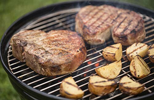 Steaks and potatoes grilling on a barbecue.