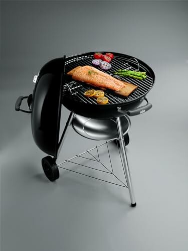 Portable charcoal grill with salmon, vegetables, and lemons.